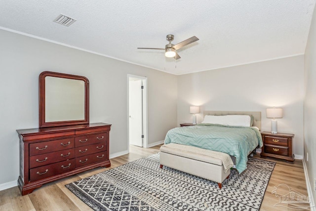 bedroom featuring light wood finished floors, baseboards, visible vents, and a textured ceiling