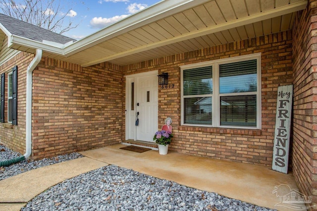 view of exterior entry with roof with shingles and brick siding