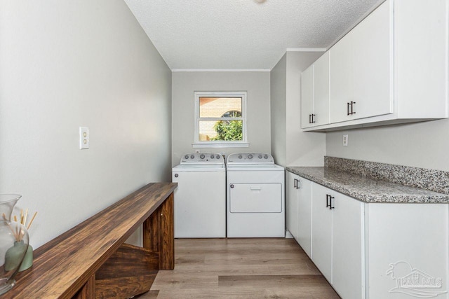 laundry room featuring cabinet space, light wood-style flooring, a textured ceiling, and washing machine and clothes dryer