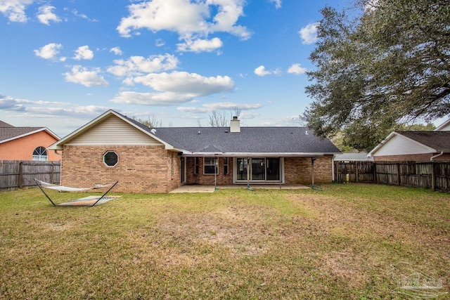 rear view of house with brick siding, a patio, a chimney, a lawn, and a fenced backyard