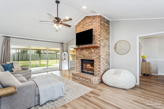 living area featuring lofted ceiling, ceiling fan, wood finished floors, crown molding, and a fireplace