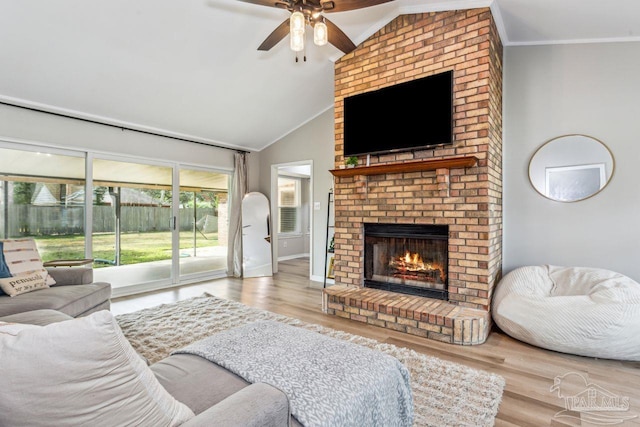 living area with lofted ceiling, a brick fireplace, crown molding, and wood finished floors