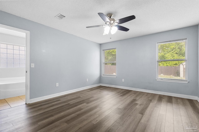 empty room with dark wood finished floors, visible vents, baseboards, a textured ceiling, and ceiling fan