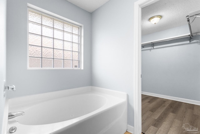 bathroom with a bath, a textured ceiling, baseboards, wood finished floors, and a walk in closet