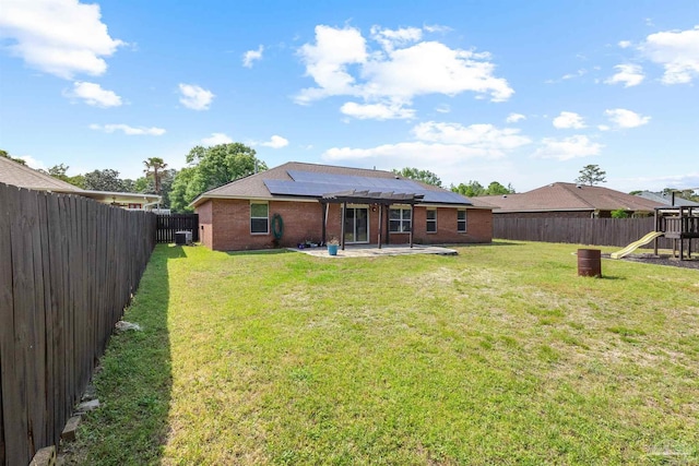 back of property with roof mounted solar panels, a playground, a fenced backyard, a patio, and brick siding
