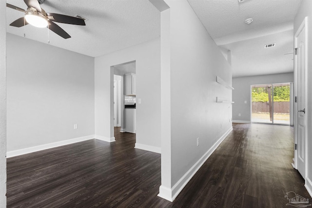hallway with dark wood finished floors, baseboards, visible vents, and a textured ceiling