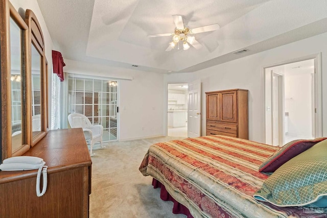 bedroom featuring a textured ceiling, a raised ceiling, connected bathroom, and light carpet