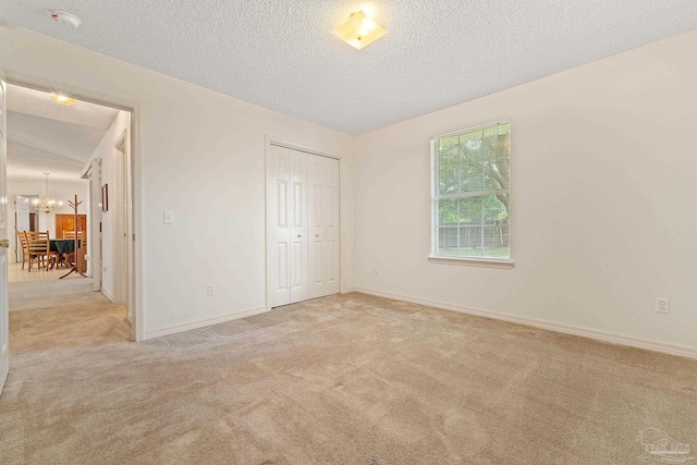 unfurnished bedroom with a textured ceiling, carpet, baseboards, and a chandelier