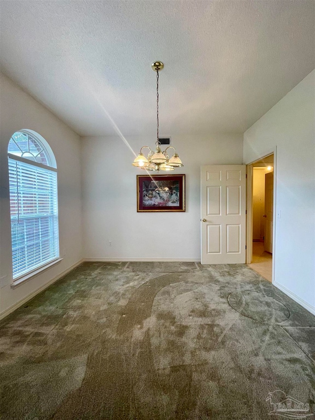 unfurnished dining area with a textured ceiling, a notable chandelier, and carpet floors