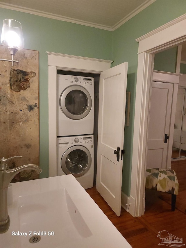 laundry area featuring dark wood finished floors, crown molding, stacked washer and dryer, and a sink