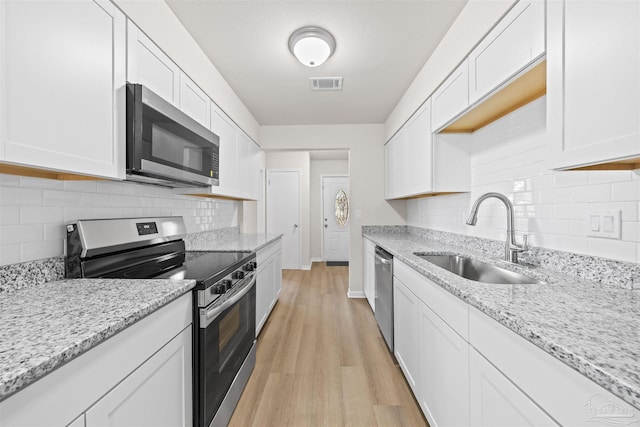 kitchen featuring white cabinets, a sink, appliances with stainless steel finishes, visible vents, and light wood finished floors
