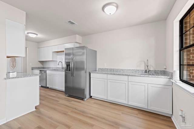 kitchen with appliances with stainless steel finishes, light wood finished floors, white cabinets, and a sink