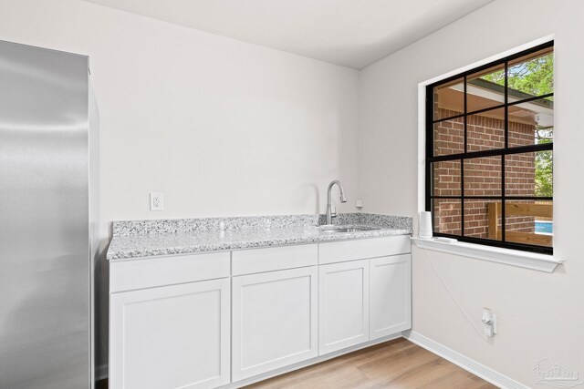 interior space featuring baseboards, freestanding refrigerator, a sink, wet bar, and light wood-type flooring