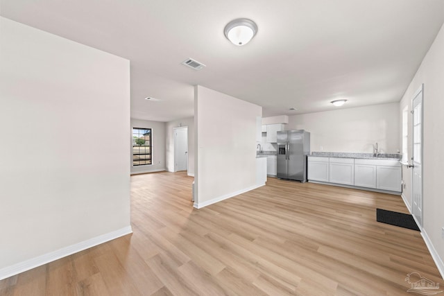 unfurnished living room featuring a sink, visible vents, light wood finished floors, and baseboards