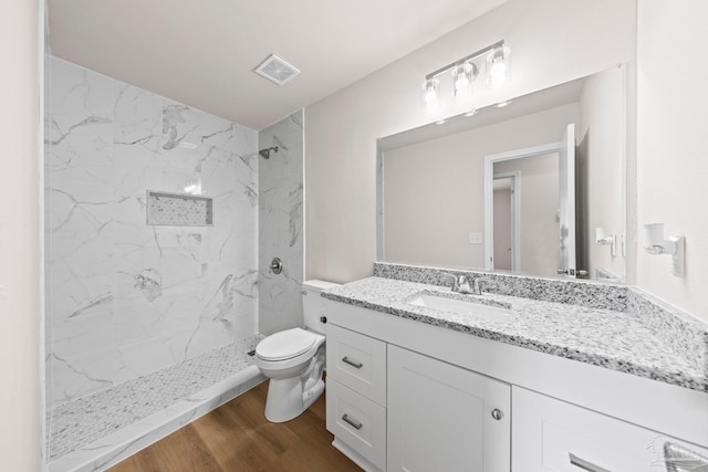 bathroom featuring wood finished floors, toilet, vanity, visible vents, and a marble finish shower