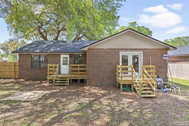 rear view of property with fence, brick siding, a shingled roof, and a wooden deck