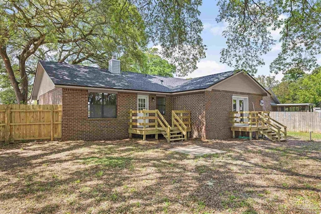 rear view of house featuring a deck, a chimney, roof with shingles, fence, and brick siding