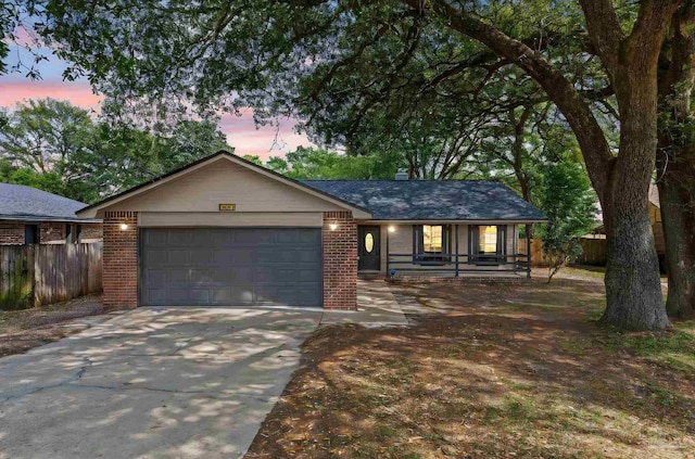 ranch-style house featuring a porch, driveway, brick siding, an attached garage, and fence