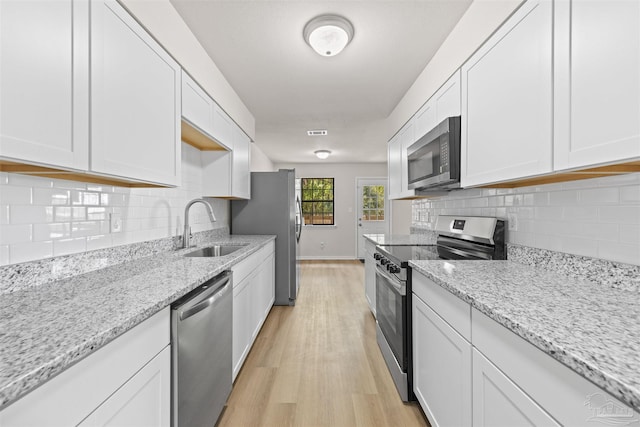kitchen featuring light wood-style flooring, decorative backsplash, appliances with stainless steel finishes, white cabinets, and a sink