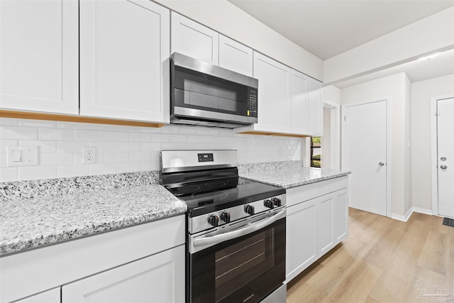 kitchen with light wood-style floors, stainless steel appliances, white cabinetry, and backsplash