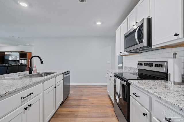 10985 Blacktail Loop, Pensacola, FL 32526 - kitchen with appliances with stainless steel finishes, a sink, white cabinets, light wood finished floors, and backsplash