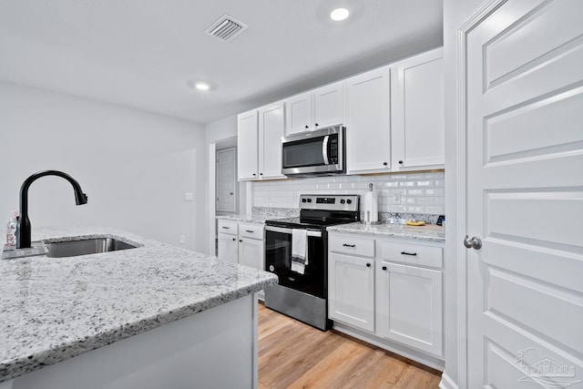 10985 Blacktail Loop, Pensacola, FL 32526 - kitchen with appliances with stainless steel finishes, a sink, white cabinets, light wood-style flooring, and decorative backsplash