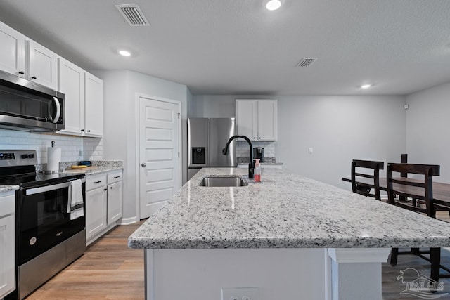 10985 Blacktail Loop, Pensacola, FL 32526 - kitchen with appliances with stainless steel finishes, a sink, a kitchen island with sink, tasteful backsplash, and light stone counters
