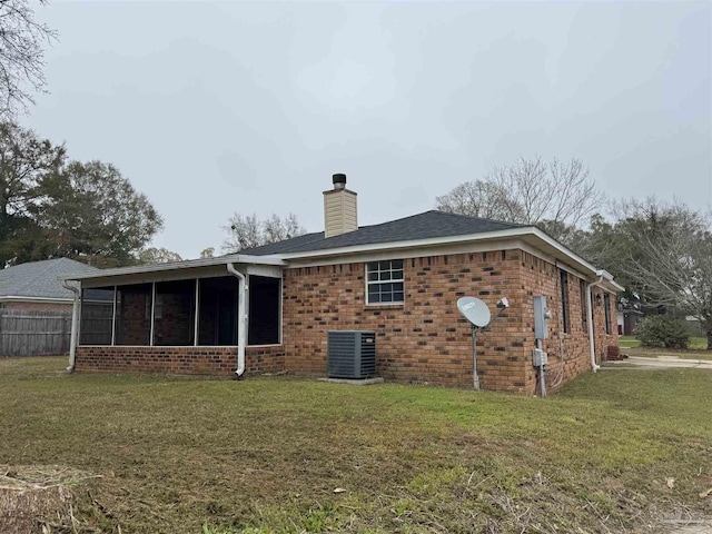 rear view of property with a yard, a sunroom, brick siding, central AC unit, and a chimney