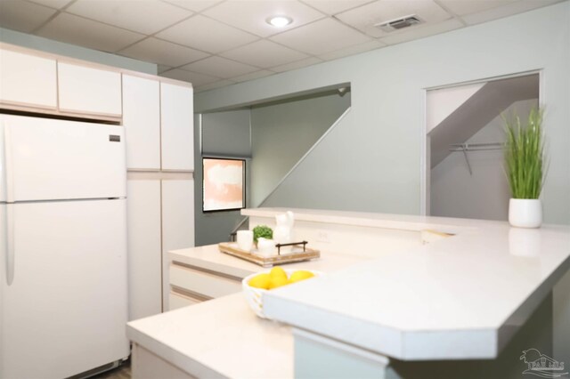 kitchen featuring white cabinets, white fridge, kitchen peninsula, and a paneled ceiling