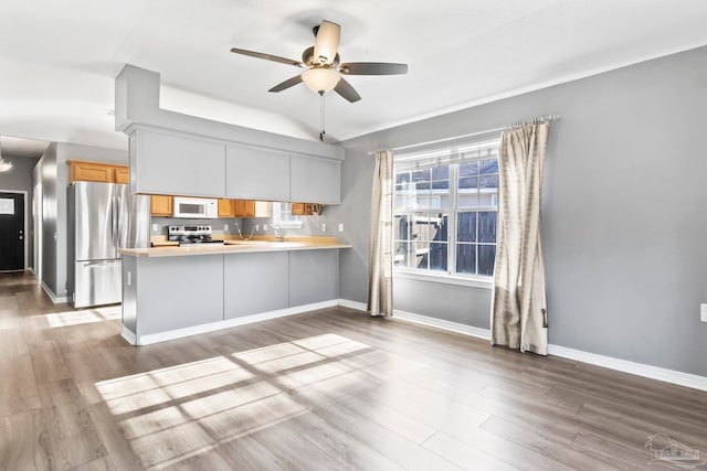 kitchen with appliances with stainless steel finishes, kitchen peninsula, white cabinets, ceiling fan, and light hardwood / wood-style floors