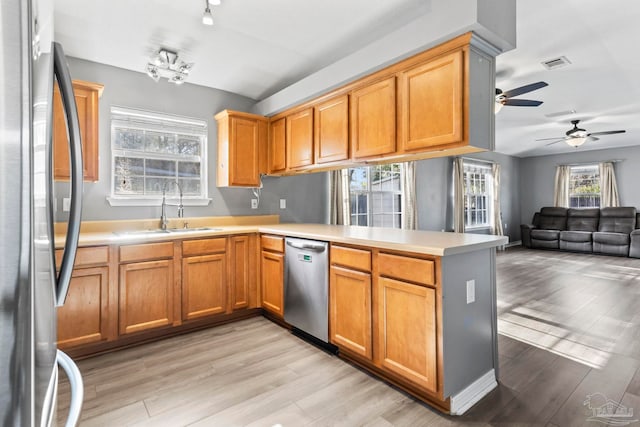 kitchen featuring sink, stainless steel appliances, light hardwood / wood-style floors, vaulted ceiling, and kitchen peninsula