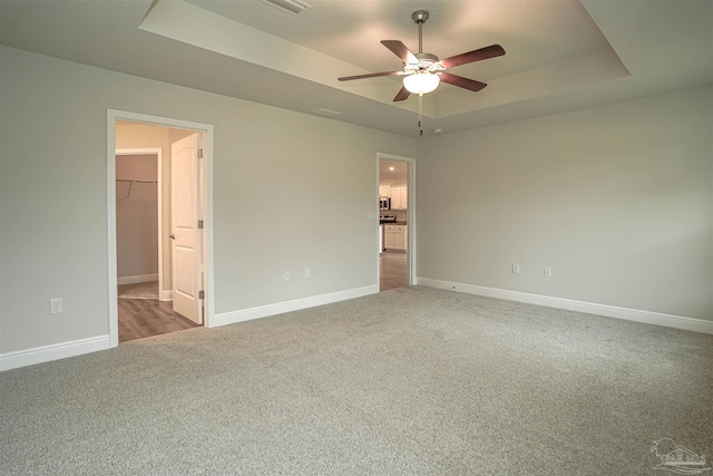 unfurnished bedroom featuring carpet flooring, a raised ceiling, ceiling fan, a spacious closet, and a closet