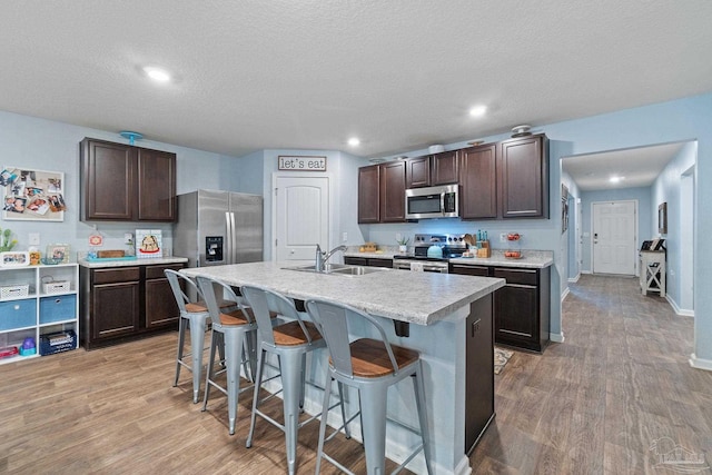 kitchen with a breakfast bar area, dark brown cabinetry, light wood-style floors, and appliances with stainless steel finishes
