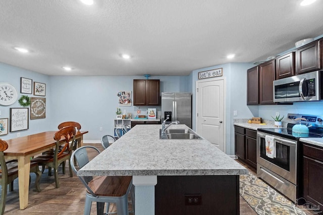 kitchen with a sink, dark wood-style flooring, stainless steel appliances, dark brown cabinetry, and light countertops
