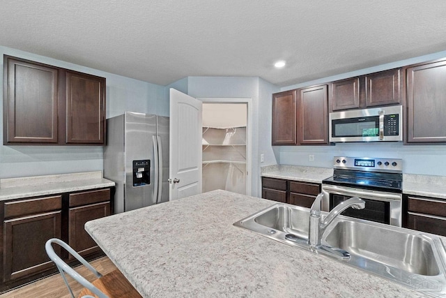 kitchen with light wood-style floors, appliances with stainless steel finishes, light countertops, dark brown cabinets, and a sink