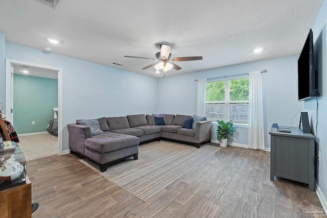 living room with a ceiling fan, visible vents, a textured ceiling, and light wood-type flooring