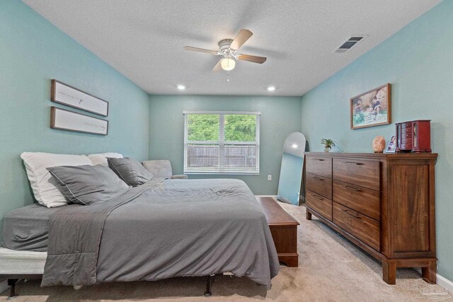 bedroom featuring a textured ceiling, visible vents, ceiling fan, and light carpet