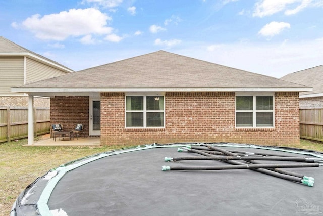 rear view of property featuring a patio, a shingled roof, a fenced backyard, and brick siding