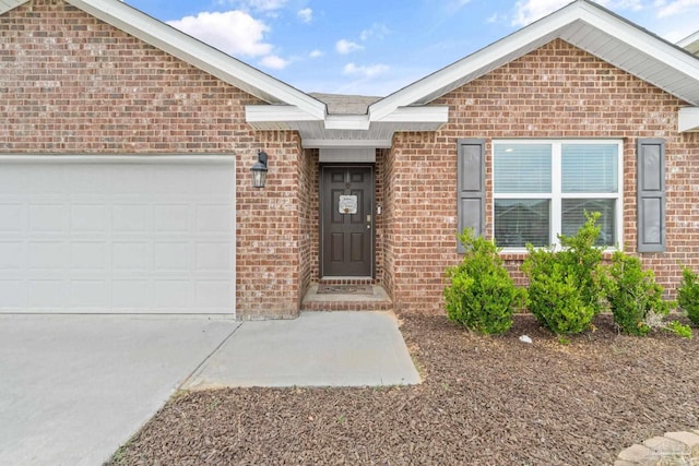 view of exterior entry with driveway, a garage, and brick siding