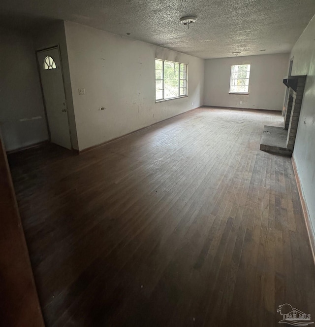 unfurnished living room with dark hardwood / wood-style flooring, a textured ceiling, and a brick fireplace