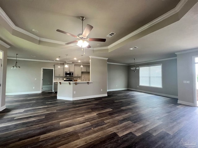 unfurnished living room with ornamental molding, a tray ceiling, ceiling fan with notable chandelier, and dark hardwood / wood-style flooring