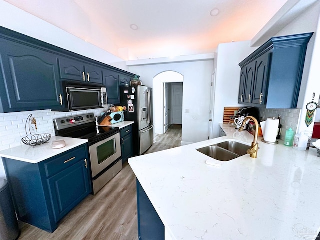 kitchen with arched walkways, light countertops, appliances with stainless steel finishes, and a sink