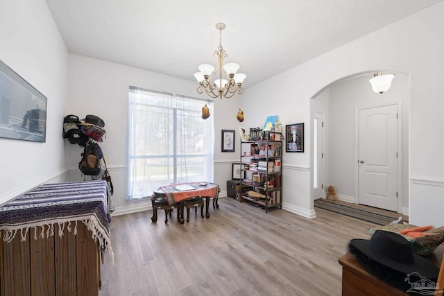 dining space featuring an inviting chandelier, light wood-style flooring, arched walkways, and baseboards