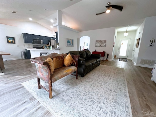 living area featuring arched walkways, wood finished floors, lofted ceiling, and visible vents