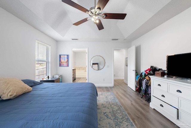 bedroom with visible vents, a tray ceiling, light wood-style flooring, and baseboards