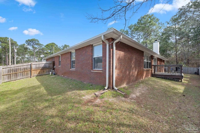 view of property exterior with brick siding, fence, a yard, a wooden deck, and a chimney