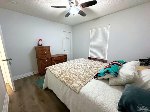 bedroom with a ceiling fan, a textured ceiling, baseboards, and dark wood-type flooring