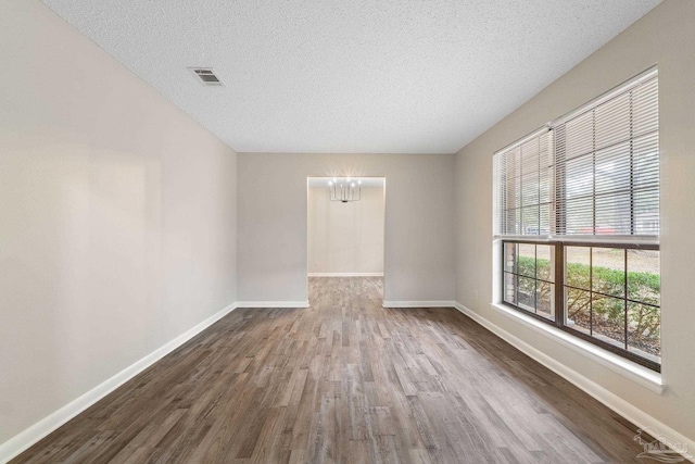 empty room featuring a notable chandelier, wood-type flooring, and a textured ceiling