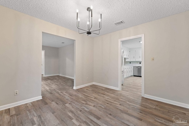 unfurnished dining area with a textured ceiling, light hardwood / wood-style floors, and a notable chandelier