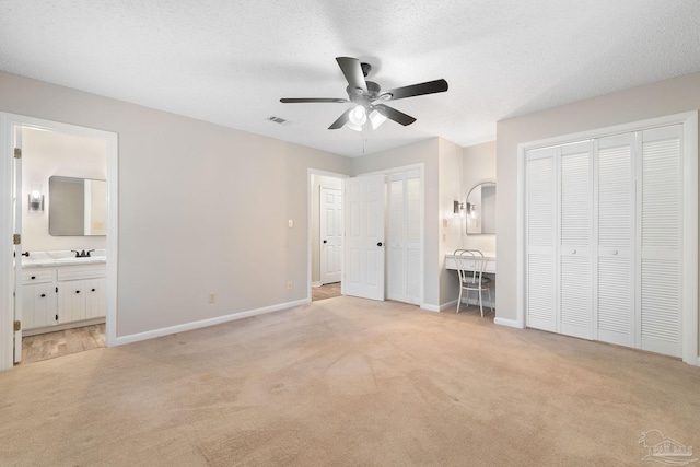 unfurnished bedroom with ceiling fan, light colored carpet, ensuite bathroom, and two closets